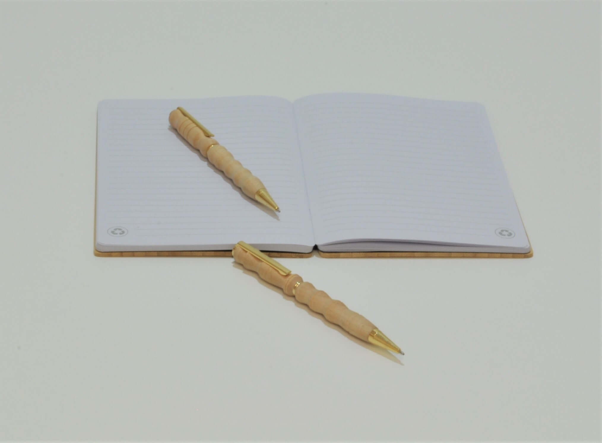 Zwei gedrechselte Holz-Kugelschreiber mit goldfarbenen Beschlägen, einer auf einem Notizbuch.